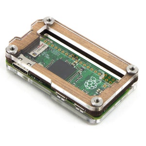 May include: A small, rectangular circuit board with a green surface, featuring a Raspberry Pi logo, is encased in a clear acrylic and wood frame. The frame is secured with silver screws. The board has various ports and a black central component.