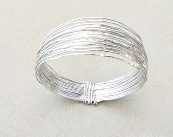 May include: A silver bracelet made of multiple thin, interwoven wires. The bracelet is circular and has a smooth, polished finish.