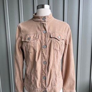 May include: A tan corduroy jacket with a stand-up collar and button-down closure. The jacket has two chest pockets and long sleeves with buttoned cuffs. The jacket is displayed on a mannequin.