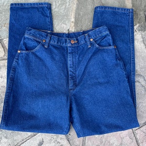 May include: A pair of classic, high-waisted, dark blue denim jeans. The jeans feature a button and zipper closure, front and back pockets, and copper-colored rivets. The straight-leg design is visible in this close-up shot.