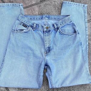 May include: Light blue denim jeans with a classic five-pocket design. The jeans have a button and zipper closure, belt loops, and a faded wash. The brand name is visible on the front pocket. A casual, everyday wear item.