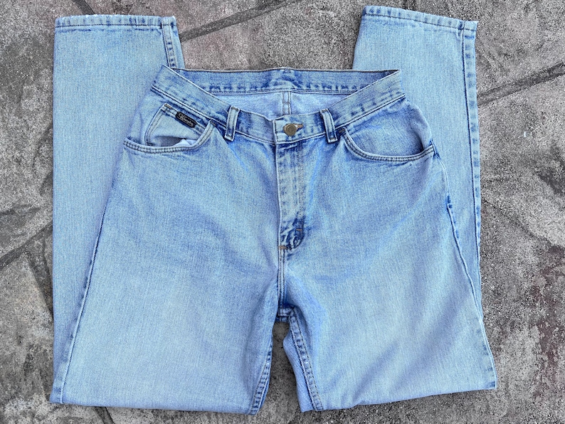 May include: Light blue denim jeans with a classic five-pocket design. The jeans have a button and zipper closure, belt loops, and a faded wash. The brand name is visible on the front pocket. A casual, everyday wear item.