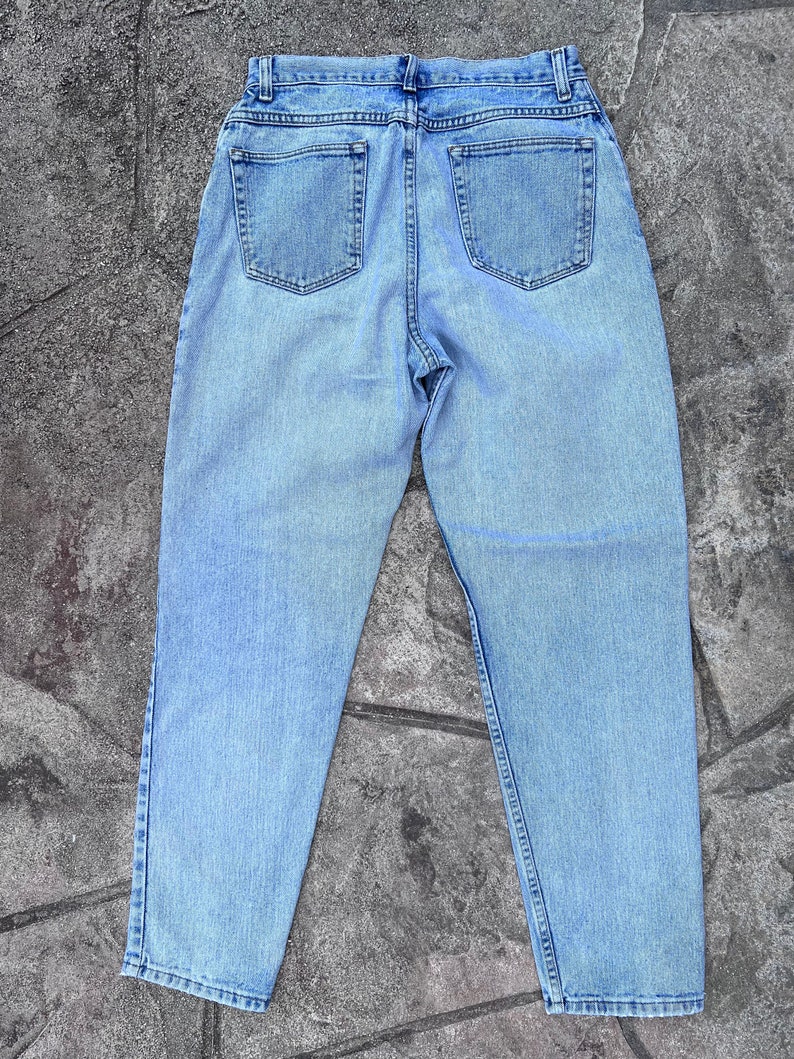 May include: Light blue denim jeans with a classic five-pocket design. The jeans have a high waist and a relaxed fit, with a faded wash for a vintage look. The back view shows the pockets and the stitching details.