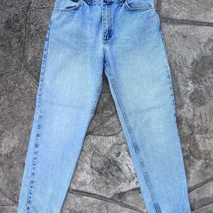 May include: Light blue denim jeans with a classic five-pocket design. The jeans have a straight leg cut and a button and zipper closure. The Lee logo is visible on the front pocket. The jeans are made of a durable denim material.
