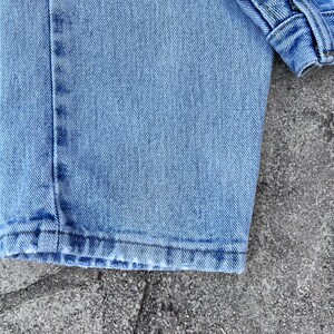 May include: Close-up of light blue denim jeans. The image shows the hem of the jeans, the stitching, and the texture of the fabric. The jeans are slightly faded, suggesting wear.