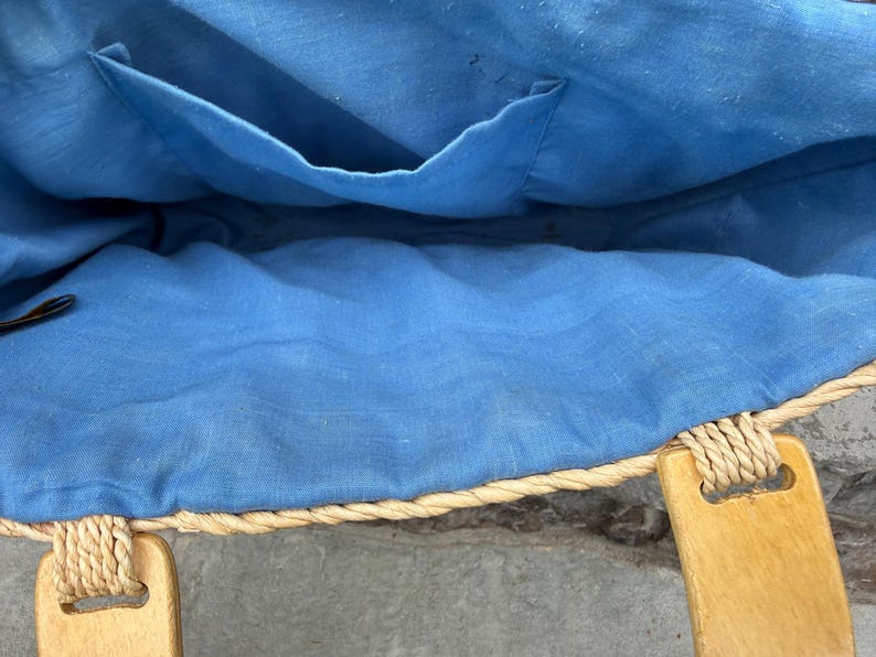 K&ouml;nnte beinhalten: Innenansicht einer Stroh-Tragetasche mit hellblauem Innenfutter und einer kleinen Tasche. Die Tasche hat Holzgriffe und eine geflochtene Seilborte. Der Innenstoff ist einfarbig hellblau.