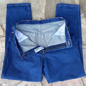 May include: Blue denim jeans with a zipper fly and button closure. The jeans are a classic straight-leg style, with a visible brand label. The denim has a medium wash, and the jeans are laid flat.