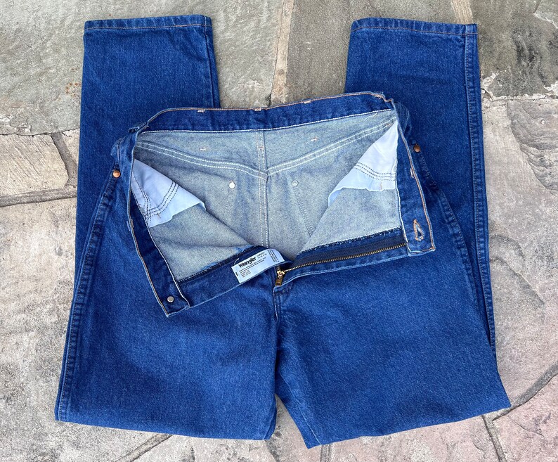 May include: Blue denim jeans with a zipper fly and button closure. The jeans are a classic straight-leg style, with a visible brand label. The denim has a medium wash, and the jeans are laid flat.