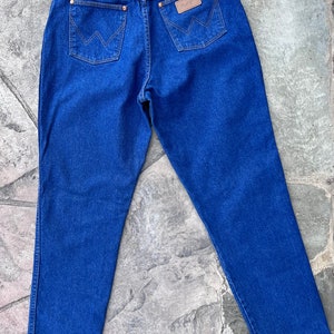 May include: Blue denim jeans with the Wrangler logo on the back pocket. The jeans have copper-colored rivets and a leather patch. The back pockets feature the Wrangler 'W' stitching.