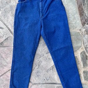 May include: A pair of classic blue denim jeans. The jeans have a high waist, straight leg, and feature gold-colored rivets and a button closure. The denim is a solid, medium-wash blue.