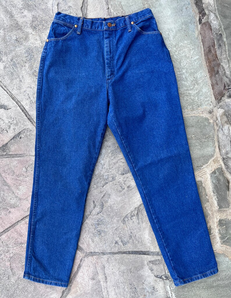 May include: A pair of classic blue denim jeans. The jeans have a high waist, straight leg, and feature gold-colored rivets and a button closure. The denim is a solid, medium-wash blue.