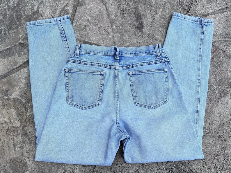 May include: Light blue denim jeans with a classic five-pocket design. The jeans are laid flat, showcasing the back pockets and the overall light wash. The fabric appears to be a medium weight denim.