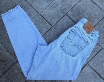 May include: Light blue denim jeans with a classic five-pocket design. The jeans feature a brown leather patch on the back and a signature Levi's back pocket stitch. The jeans are folded and laid flat.