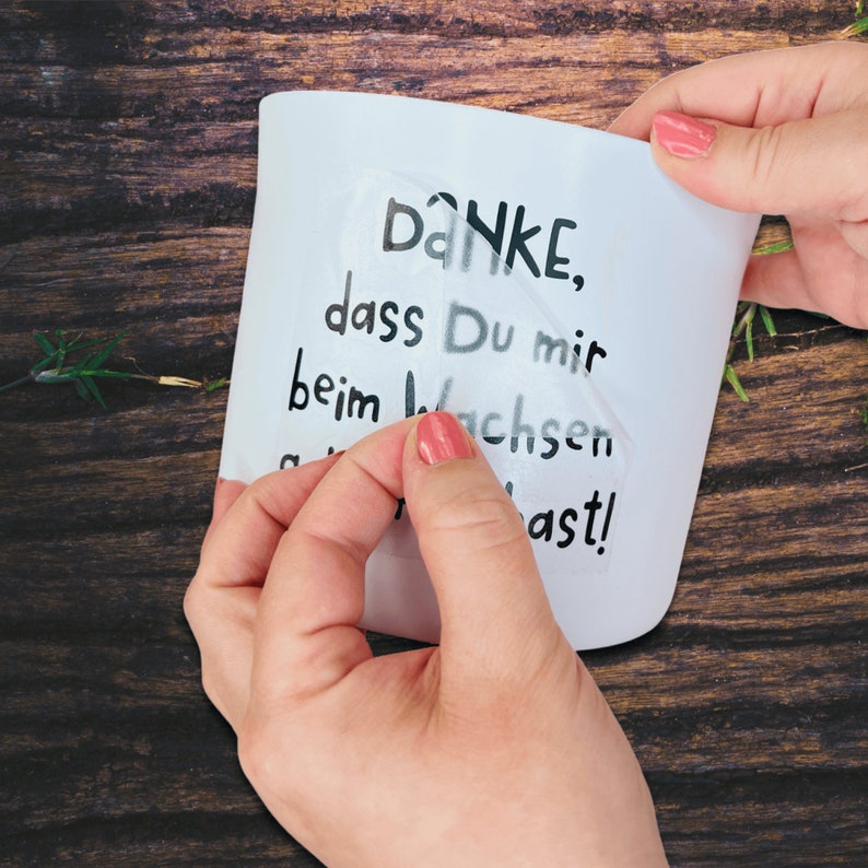 May include: A white mug with a black vinyl sticker that says "DANKE, dass Du mir beim wachsen  hast!"