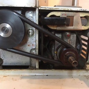 Peut inclure: Gros plan sur le mécanisme interne d'une machine à coudre, montrant une courroie noire reliant un moteur à une poulie. Le moteur est marqué "BERNINA".