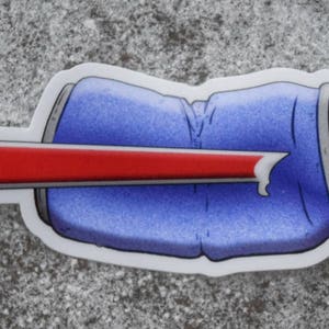 Puede incluir: Una lata de aluminio azul con una franja roja en el medio. La lata está aplastada y tiene un agujero en el lateral.