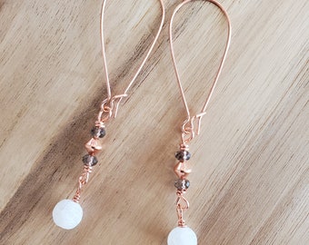 Puede incluir: Un par de pendientes colgantes de oro rosa con cuentas blancas y marrones. Los pendientes tienen un diseño simple y elegante.
