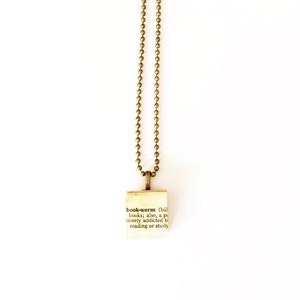 May include: A gold chain necklace with a small pendant featuring the definition of the word "bookworm".