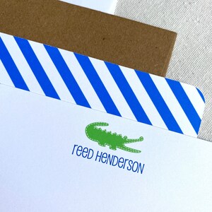 May include: White stationery with blue and white striped border. A green alligator illustration and the text "reed Henderson" are printed on the stationery.