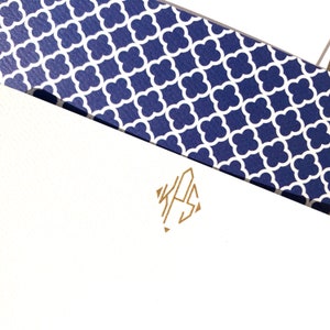 May include: White stationery with a gold monogram of the letters "KHS" in a diamond shape. The stationery is topped with a blue and white patterned paper.