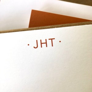 May include: A white card with a brown border and the text ". JHT ." printed in red.