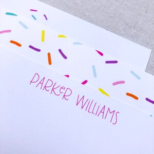 May include: White stationery with a pink, orange, yellow, blue, and purple confetti pattern. The name "Parker Williams" is printed in pink at the bottom of the card.