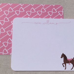 May include: Two notecards. The top card has a pink background with a white equestrian bit pattern. The bottom card is white with the name "evie williams" in cursive and a brown horse illustration with a pink saddle.