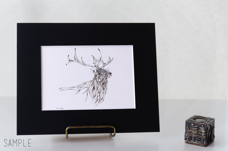 May include: A framed art print featuring a detailed black and white illustration of a stag with large antlers. The artwork is displayed in a black mat and frame, resting on a brass easel. The word "SAMPLE" is printed at the bottom.