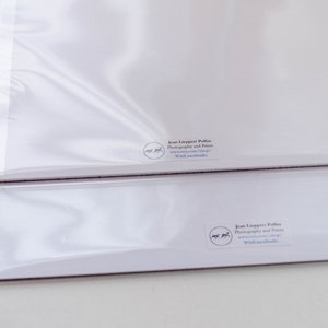May include: Two white art prints in clear protective sleeves. The prints have a small circular logo and text in the lower right corner. The prints are stacked on top of each other.