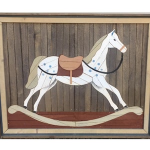 May include: A white rocking horse with blue spots and a brown saddle is painted on a wooden background. The horse is framed in a brown wood frame.