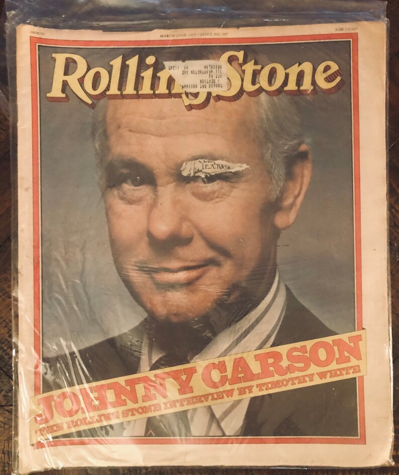 May include: A vintage Rolling Stone magazine cover featuring Johnny Carson. The cover is yellowed with age and has a small piece of tape over Carson's eye. The text on the cover reads "Johnny Carson" and "The Rolling Stone Interview by Timothy White."