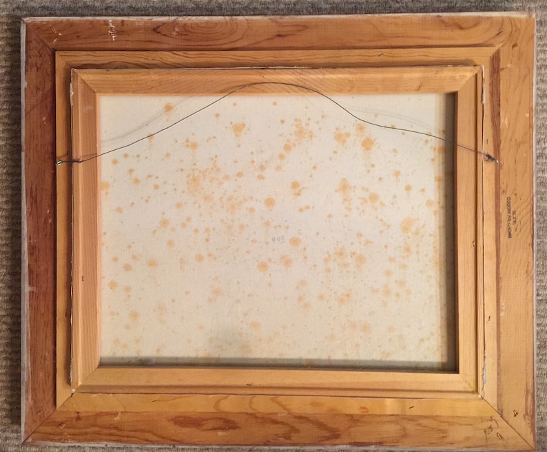 May include: The back of a framed painting with a light brown wooden frame. The canvas is a light beige color with some brown stains.