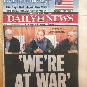 May include: A black and white newspaper front page with the headline "'WE'RE AT WAR'" and a photo of three men in suits. The newspaper is titled "DAILY NEWS" and the date is September 16, 2001.