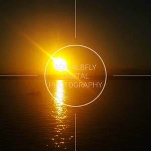 以下が含まれることがあります： 水域の上に明るいオレンジ色の夕焼けがあり、中央に「SOCIALBFLY DIGITAL PHOTOGRAPHY」というテキストが入った白い円があります。