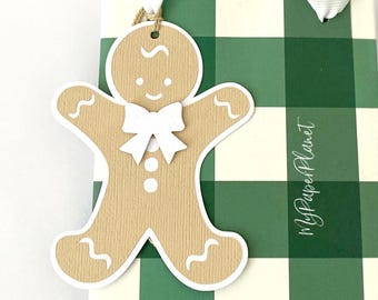May include: A tan gingerbread man paper tag with white icing details and a white bow, attached to a green and white checkered gift bag featuring the text MyPaperPlanet printed vertically in white script on the right side of the bag.