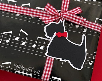 May include: A wrapped gift with black paper printed with musical notes. A red and white checkered ribbon is tied around the gift, with a black dog-shaped tag with a red bow. The tag has a white border.