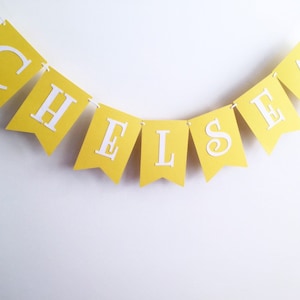 May include: A yellow banner with the name "Chelsea" spelled out in white letters.