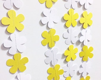 May include: A garland of alternating yellow and white paper flowers. The flowers are connected by a white string.