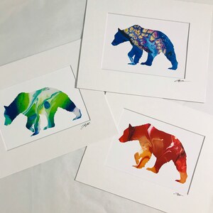 May include: Three framed art prints featuring bear silhouettes with abstract, colorful designs. One bear is blue with yellow and purple accents, another is green and blue, and the third is red and orange. Each print is matted in white.