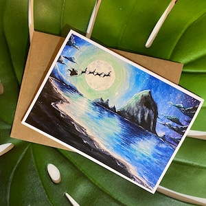 May include: A Christmas-themed greeting card featuring a watercolor painting of Santa Claus in his sleigh, pulled by reindeer, flying over a snowy landscape under a full moon. The card is paired with a brown envelope.