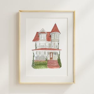 May include: Watercolor painting of a house with a red roof and a turret. The house has a light green exterior, a porch, and is framed in a light wood frame. Green shrubbery is visible around the base of the house.