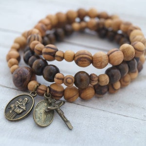 May include: A triple-strand bracelet made of brown and light brown wooden beads with a metal charm of two figures and a crucifix.