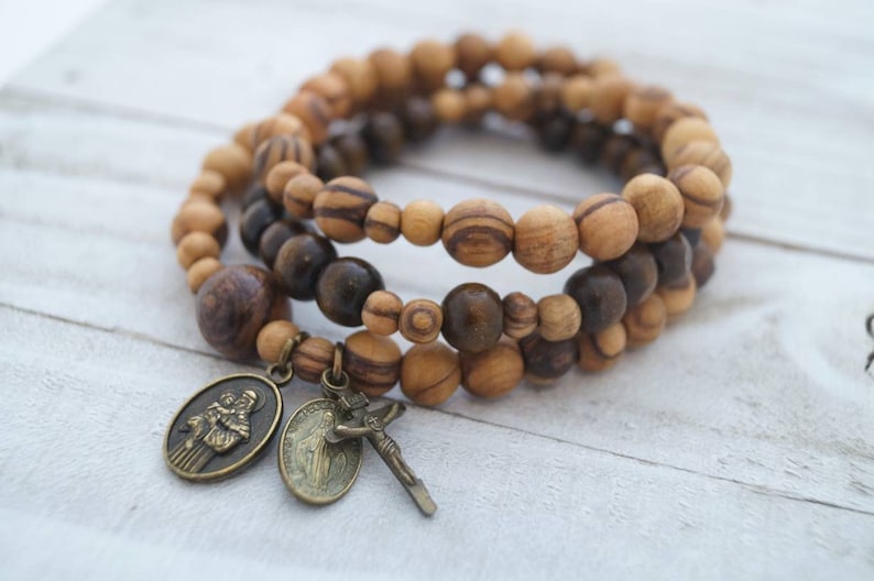 May include: A triple-strand bracelet made of brown and light brown wooden beads with a metal charm of two figures and a crucifix.