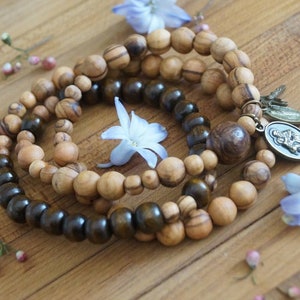 May include: Three wooden beaded bracelets with a silver charm. The bracelets are made of dark brown and light brown wood beads. The charm is a silver oval with a religious image.