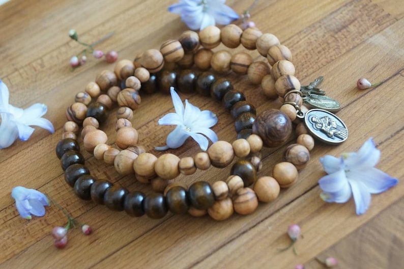 May include: Three wooden beaded bracelets with a silver charm. The bracelets are made of dark brown and light brown wood beads. The charm is a silver oval with a religious image.