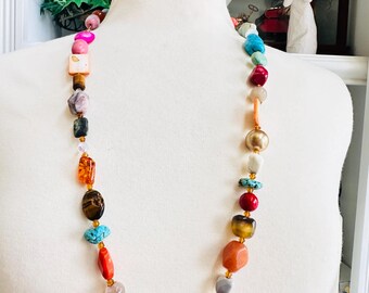 May include: A colorful beaded necklace with a variety of shapes and sizes. The necklace features a mix of gemstones and beads in shades of pink, orange, green, blue, and brown. The necklace is displayed on a white mannequin.