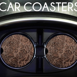May include: Two brown leather car coasters with a floral embossed design. The coasters are in a car cup holder.