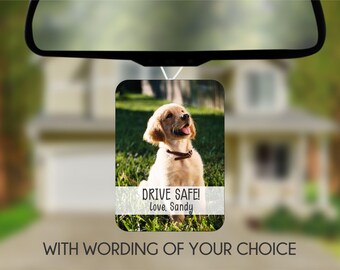 May include: A white car air freshener with a photo of a golden retriever puppy sitting in green grass. The text "DRIVE SAFE! Love, Sandy" is printed on the air freshener.