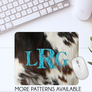 May include: A brown and white cowhide mousepad with the letters LRG in turquoise blue. The letters are stylized with a textured, almost mosaic-like appearance. The text "MORE PATTERNS AVAILABLE" is printed below the mousepad.