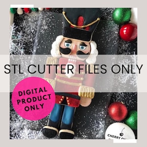 Puede incluir: Un archivo de corte STL descargable digitalmente para un cortador de galletas de cascanueces. La imagen muestra una galleta de jengibre decorada con forma de cascanueces con detalles rojos, dorados y azules. El texto "STL CUTTER FILES ONLY" y "DIGITAL PRODUCT ONLY" es visible en la imagen.